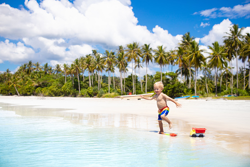 Child playing on tropical beach with palm trees. Little baby boy at sea shore. Family summer vacation. Kids play with water and sand toys. Ocean and island fun. Travel with young children in Asia.