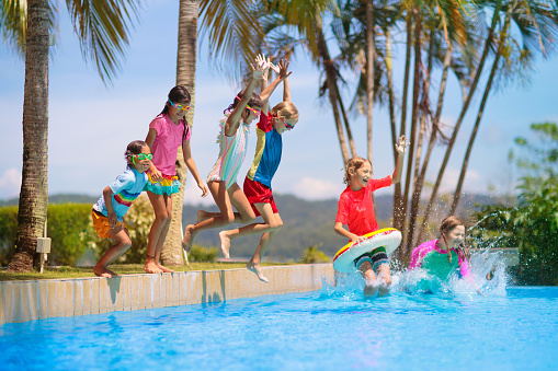 Group of kids jump into swimming pool. Summer water fun. Children play in outdoor pool. Summer family vacation with young kid. Holiday in tropical resort. Travel with child.