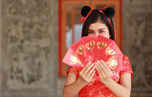 Beautiful Asian woman in red Chinese dress traditional cheongsam qipao with gesture of showing red envelope or Any Pao with exciting emotion, text means good luck entering the house (Chinese new year)