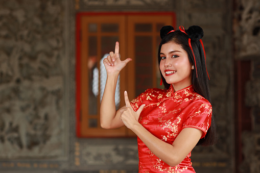 Beautiful Asian woman standing with red dress traditional cheongsam qipao and gesture of show something with happy smiling face on grey background (Chinese new year concept)