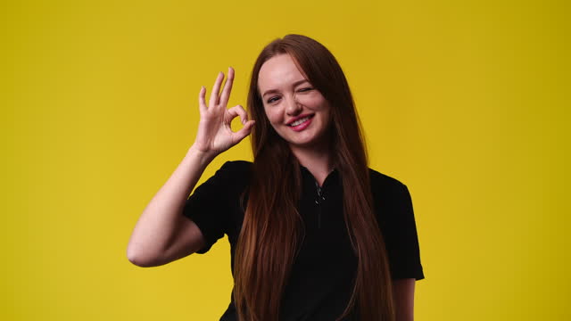 4k slow motion video of one girl showing OK sign and smiling over yellow background.