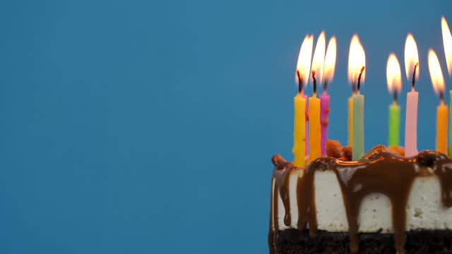 Lighted candles in a birthday cake rotation on a blue background. Candles in birthday cheesecake for home party