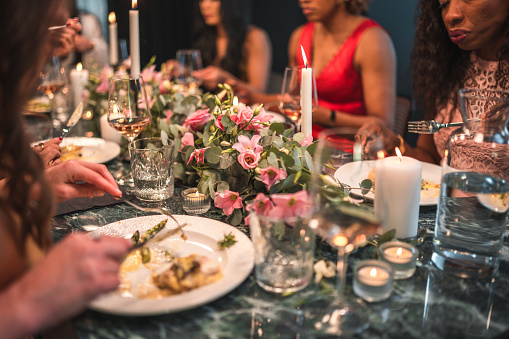 Photo of elegantly setting table at the bachelorette dinner. A small group of close multicultural female friends enjoying fine wine and delicious food.
