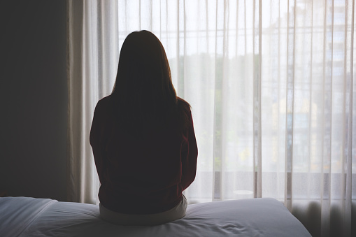 Rear view image of a woman sitting alone on a bed in bedroom