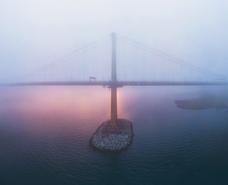 Aerial view of a harbour bridge enveloped in a fast moving fog bank during sunset.