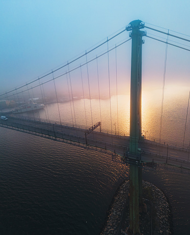 Aerial view of a harbour bridge enveloped in a fast moving fog bank during sunset.