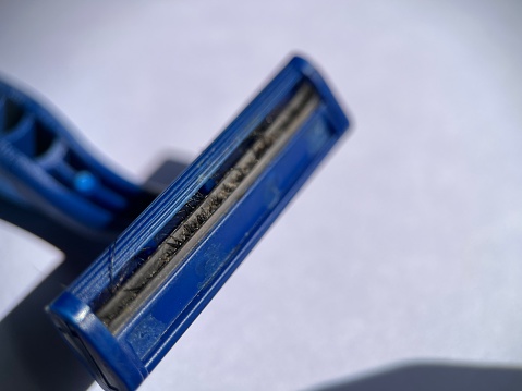 Selective focused view of dirty razor with hair stuck between blades isolated on white background. Macro photography.