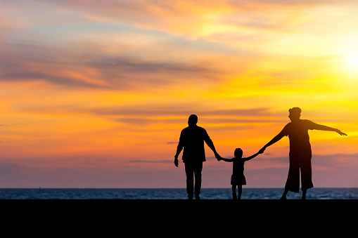 Silhouette of Family holding hands enjoying with sunset on the beach, Mom dad and daughter playing on the beach