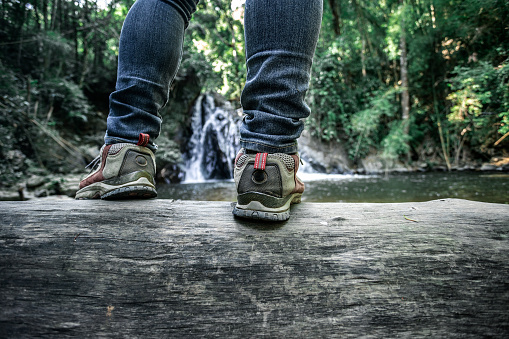 Young woman wearing jeans sneakers sitting in a river bank hanging her legs over the water