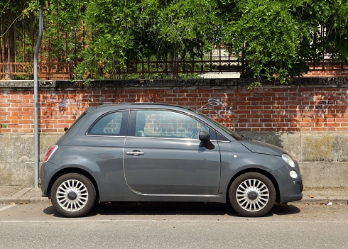 Udine, Italy. May 23, 2023 Gray new Fiat 500 at the roadside with brick wall fence on background. Side view.