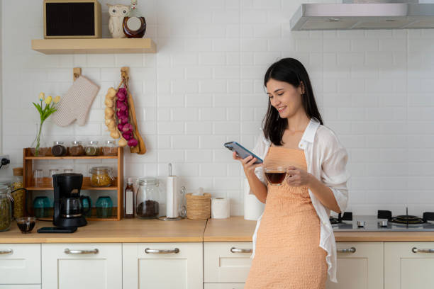 istock Young woman using smartphone leaning at kitchen table with coffee mug and modern home organizer Smiling woman reading phone message. 1493096450