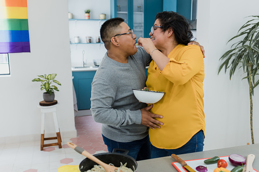 Latin lesbian couple cooking dinner in kitchen at home in Mexico, Hispanic homosexual people from lgbt community with rainbow flag in Latin America