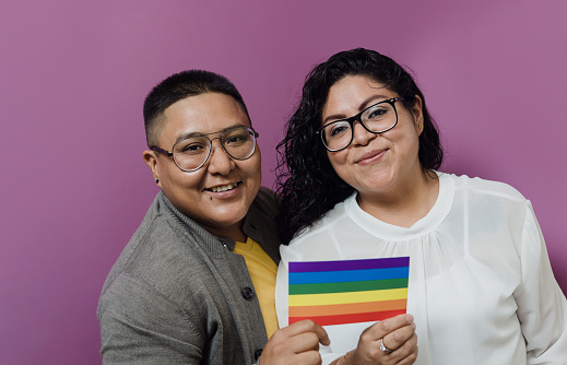 Latin Lesbian and transgender couple holding rainbow flag in Mexico, Hispanic homosexual people from lgbt community in Latin America