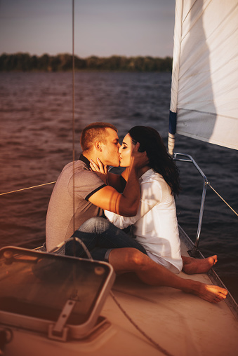Portrait of cute loving couple hugging in the white boat at sunset. Summer vacation, love, kissing, honeymoon. Beautiful view, warm sunlight, blue water of sea. emotional man and woman.