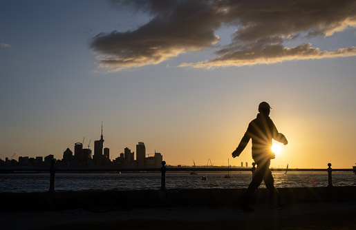 Man walking at Devonport waterfront at sunset. Skytower and Auckland cityscape in the background.