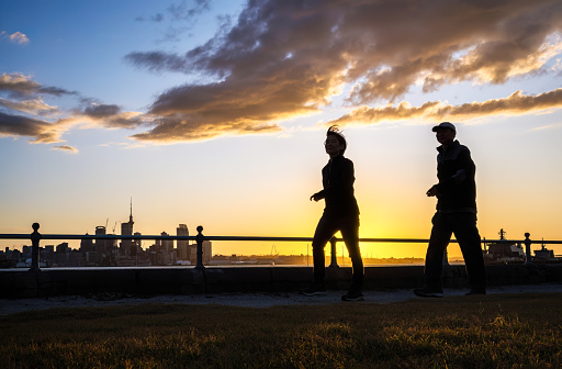 Couple walking at Devonport waterfront at sunset. Skytower and Auckland city high-rises in the background.