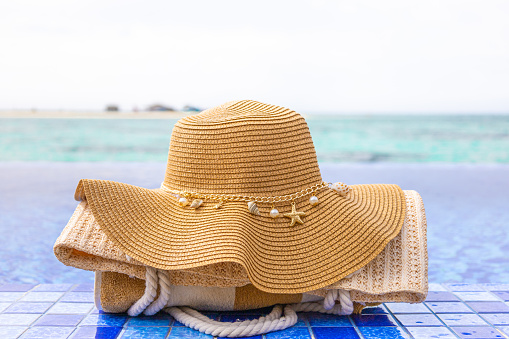 Beach hat with sea shells, towels and bag on a Maldives island resort. Summer holidays banner with crystal turquoise water. Vacation, paradise, relax, tropical, pool party and luxury travel concept.