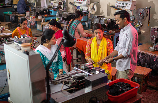 High angle view of mid adult male manager showing sample of printed fabric to female workers at textile factory