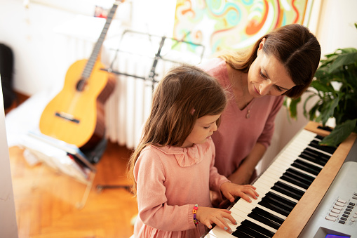 Woman and girl playing a piano. Beautiful mom teaching her daughter playing a piano.