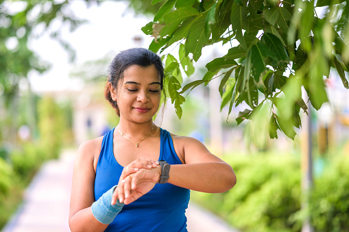 Close up shot of young sportswoman looking at smartwatch after morning exercise at park . Fitness female monitoring her progress on smartwatch.