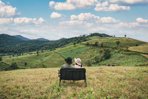 Young couple traveler relaxing with chair on mountain peak in rural scene on sunny day at summer vacation