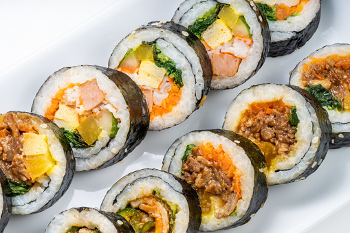 Korean Sushi Rolls or Kimbap is a popular Korean dish in white plate on wooden table, California Maki,  Steamed rice wrapped in seaweed with shrimp eggs meat and vegetable.