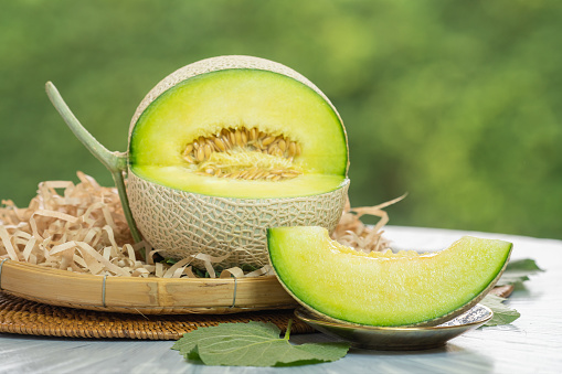 Crown Musk Melon on blurred greenery background, Cantaloupe Crown Melon fruit in Bamboo mat on wooden table in garden.