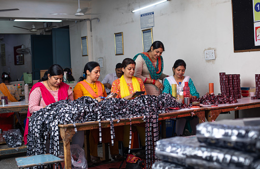 Smiling female manager inspecting and guiding workers cutting printed garments on table at textile factory and representing women empowerment