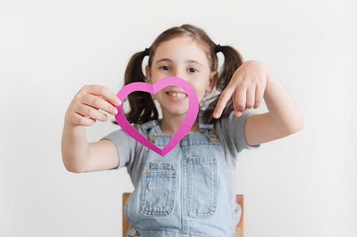 Cheerful kid holding pink heart-shape carton isolated on white