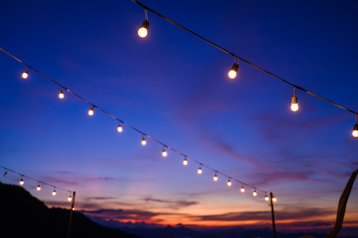 Festoon string lights decoration at the party event festival against sunset sky. light bulbs on string wire with copy space. Outdoor holiday background