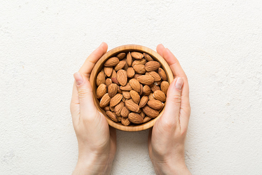 Woman hands holding a wooden bowl with almond nuts. Healthy food and snack. Vegetarian snacks of different nuts.