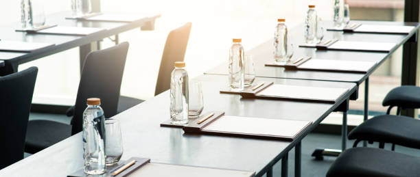 sala vacía de seminarios o reuniones de negocios en el hotel. botellas de agua de plástico, vasos con lápices y notas de papel colocadas sobre la mesa preparadas para conferencias o reuniones. - office water business meeting fotografías e imágenes de stock