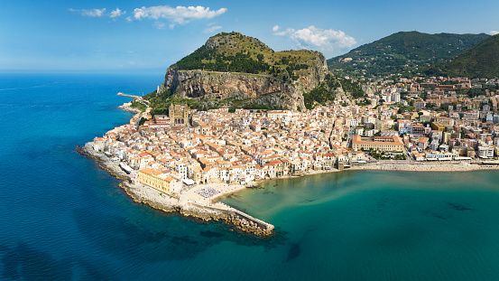 Cefalù City Aerial Drone Point of View Panorama over the turquoise mediterranean sea of north sicily’s tyrrhenian coast. Famous Cefalù Cathedral in the village center and iconic hill La Rocca in the back of Cefalu Town. Cefalu, Tyrrhenian Coast, Gibilmanna, Northern Sicily, Sicily Island, Italy, Southern Europe.