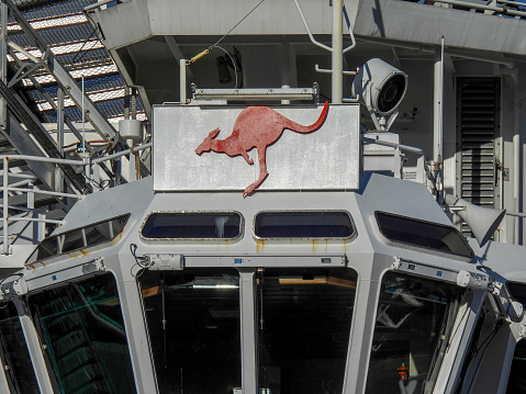 The bridge of Australian Defence Vessel (ADV) Reliant of the Royal Australian Navy docked at Garden Island Naval Base, Sydney Harbour.   The red kangaroo is the national insignia affixed to all major fleet ships.  Above the bridge, to the top left, is part of the helicopter landing platform.  This image was taken on a sunny afternoon on 20 May 2023.