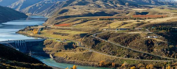istock Panoramic aerial view to Clyde dam with river and winding road on hillside surrounded by mountainous and autumn trees. 1493122658