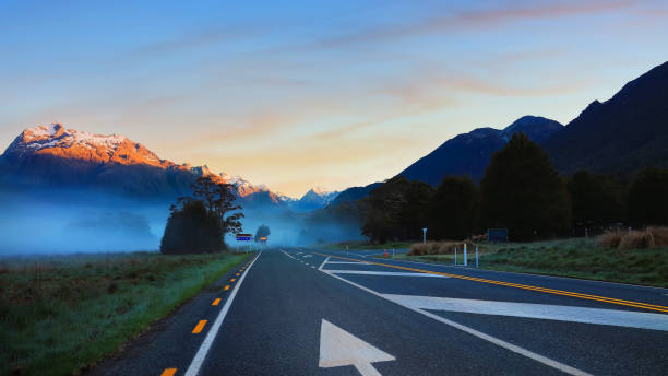 a vista de viagem de estrada da cena de viagem e nevoeiro pela manhã com cena do céu do nascer do sol no parque nacional fiordland - sunrise new zealand mountain range mountain - fotografias e filmes do acervo