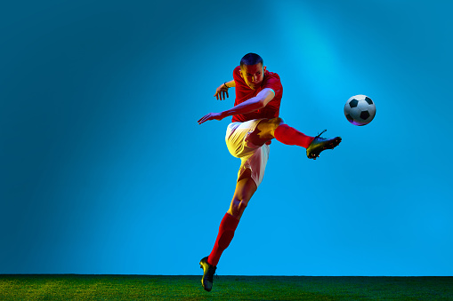 Sport betting. One young man, professional soccer football player training over soccer field background in neon light. Copy space for ad. Concept of action, energy, sport, team game