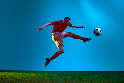Portrait with one professional football, soccer player in sportswear playing, training over field, stadium background in neon light. Concept of team game, sport, championship, competition, active, ad