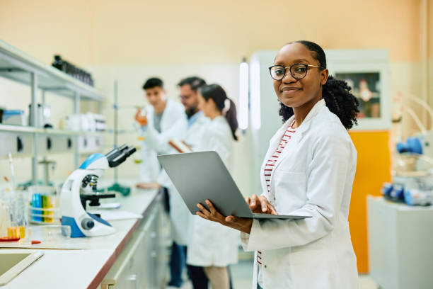 istock Happy black female chemist working on laptop in laboratory and looking at camera. 1493124887