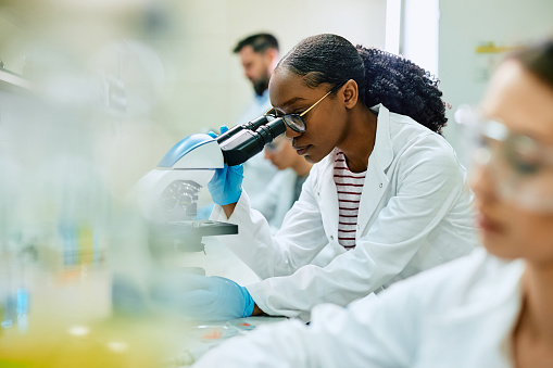 African American biochemist using microscope during scientific research in laboratory.