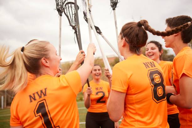 In a display of pure joy, female lacrosse players lift their sticks triumphantly in the air to celebrate their victorious game.