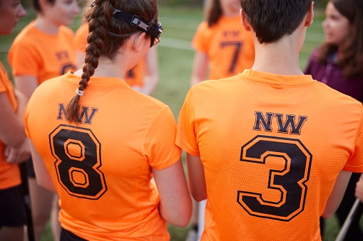 close-up shot, lacrosse players lean in, fully engrossed in their coach's instructions