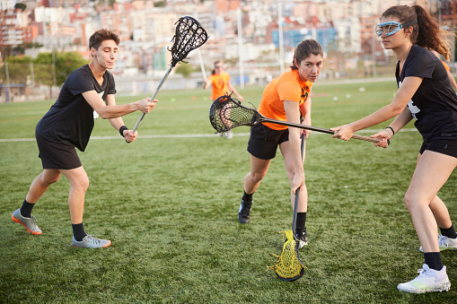 A female lacrosse player prepares to deliver a formidable free kick. With two rival defenders challenging.