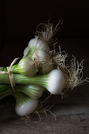 High angle view of bundle of scallions on rustic wooden table against black background