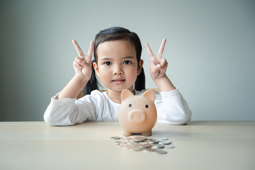 Kid holding her pink piggy bank concept of savings for future or education. Asian girl with a pink piggy bank to save for education and family expenses. Little daughter learn to save money.