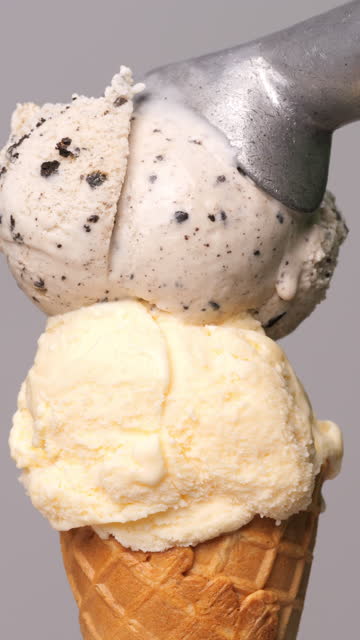 Scoop cookie ice cream on top of vanilla ice cream cone on a gray background.