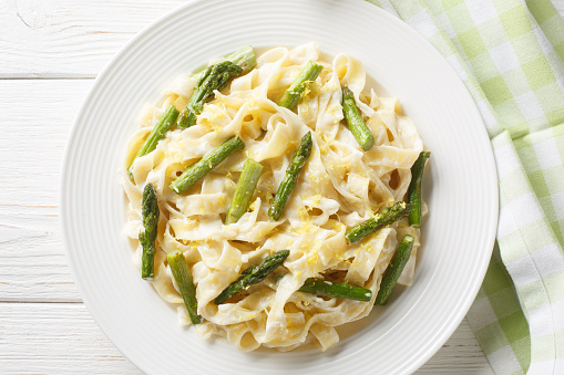 Delicious fettuccine pasta with asparagus, lemon in creamy parmesan sauce close-up in a plate on the table. Horizontal top view from above