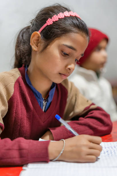 Indian girl of elementary school age studying in the classroom, wearing school uniform and writing on a notepad, learning and education concept, India.