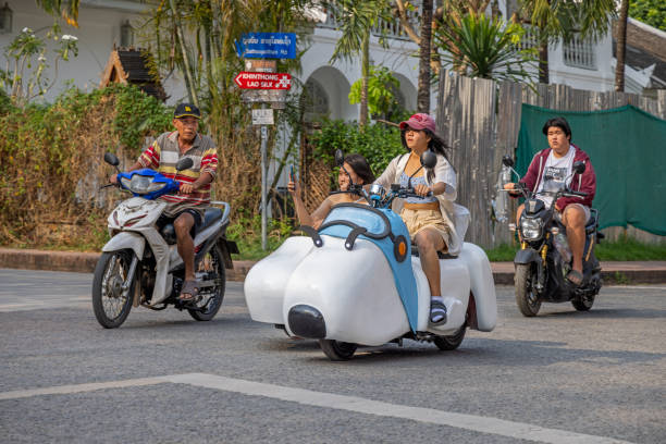 Luang Prabang, Laos - March 12th 2023: Two young female tourists on a funny motorcycle with sidecar