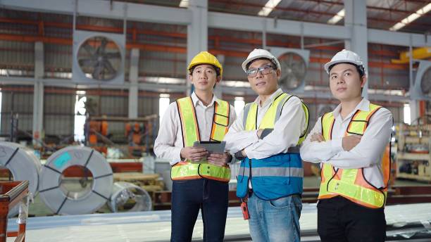 equipe de engenheiros asiáticos homens usando capacete de segurança e colete de pé com os braços cruzados na fábrica industrial. olhando em volta para a fábrica. conceito de trabalho em equipe - manager foreman warehouse arms crossed - fotografias e filmes do acervo